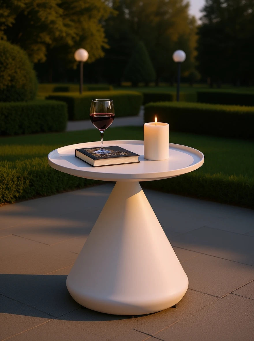 Keukenhof Spitz zulaufender Couchtisch mit gerollten Kanten, modern und minimalistisch, auf einer Terrasse. Obenauf brennt eine weiße Kerze neben einem Rotweinglas und einem geschlossenen Buch.
