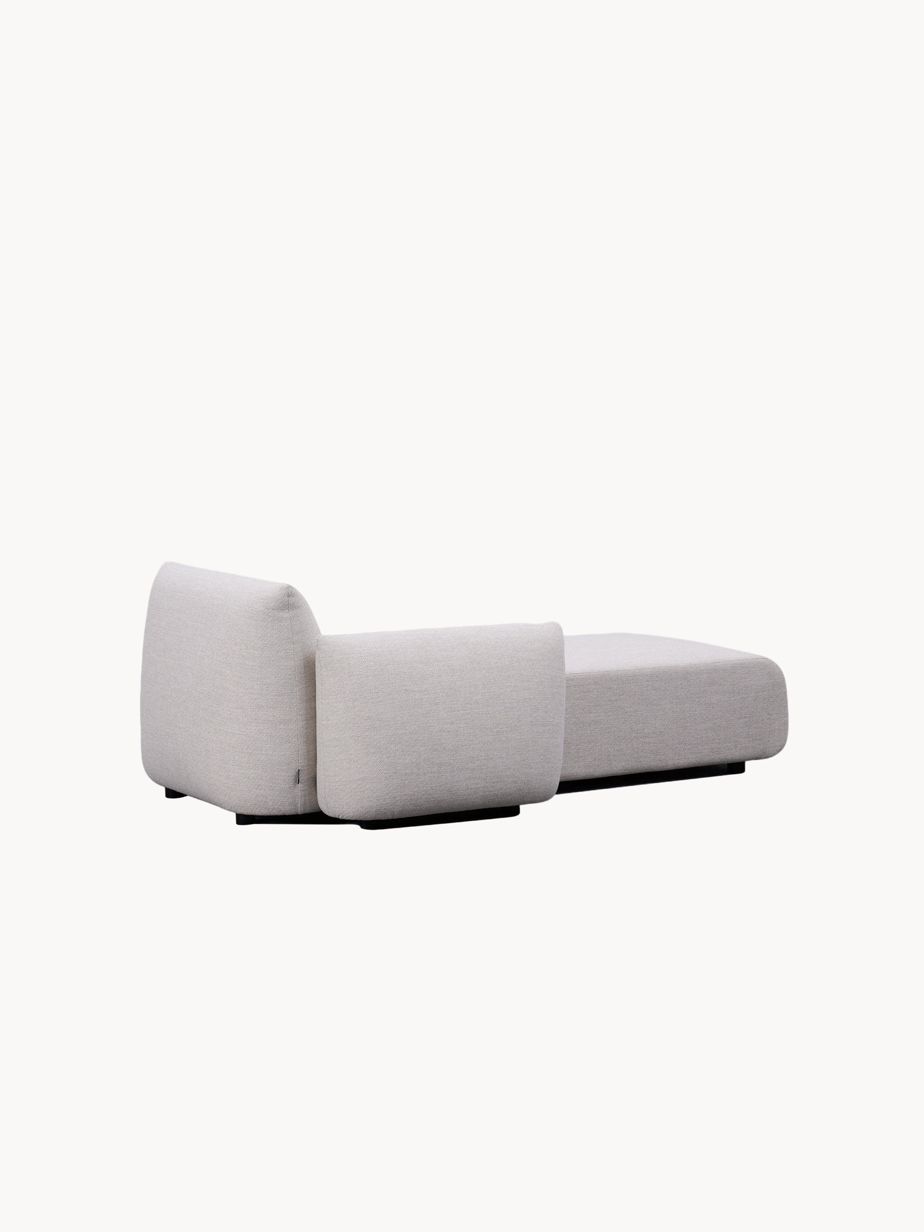 Babymax L-Lounge Set, 2er-Set: Ein modulares Loungemodul mit niedrigem Profil, gepolstert in hellem Stoff, mit abgerundeter Rückenlehne und breiter Sitzfläche auf einem schwarzen Sockel, verleiht einen schwebenden Eindruck.
