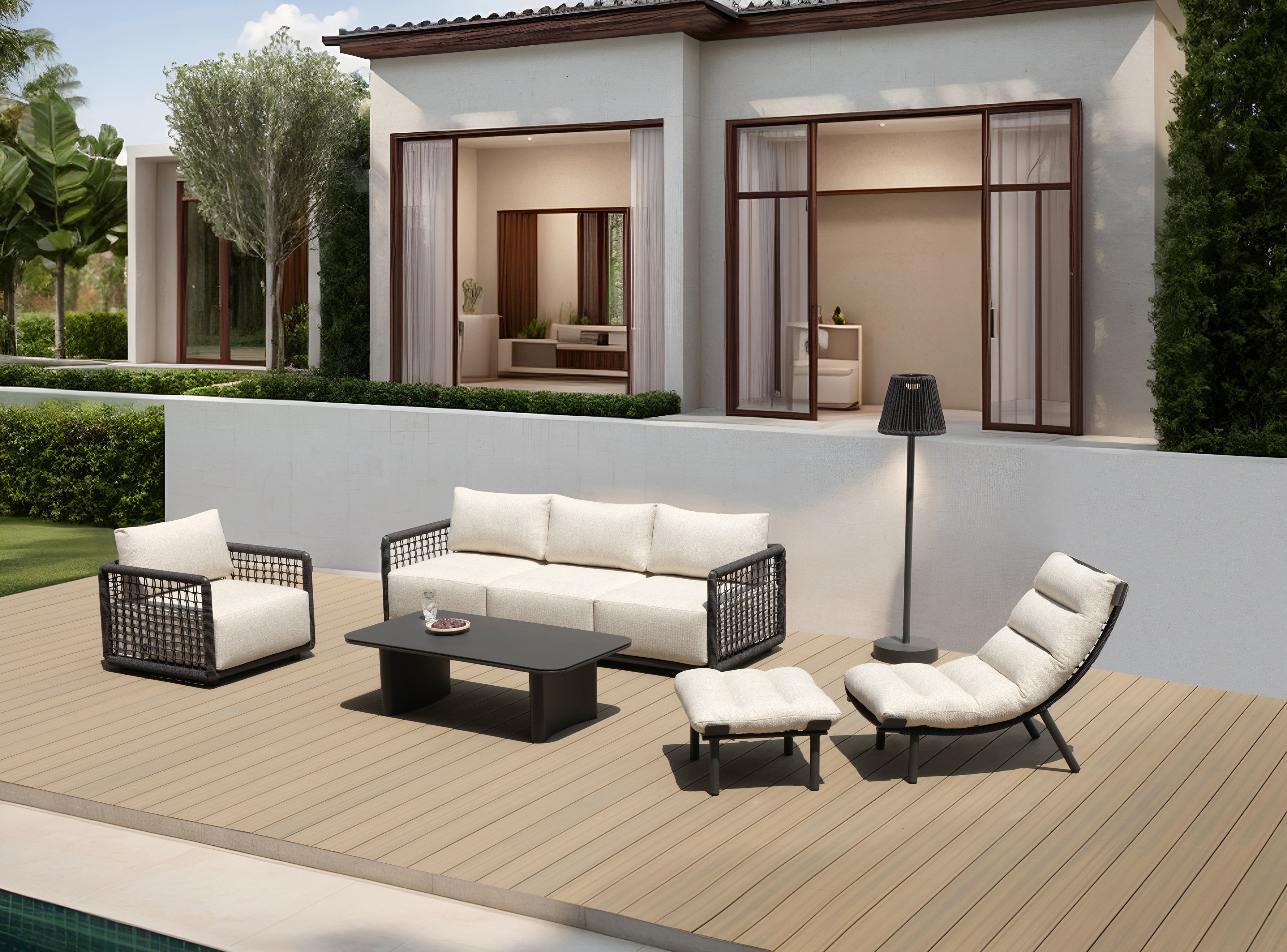 Mykonos Garten Ecklounge Set auf einer modernen Terrasse: ein dunkles Geflechtsofa mit hellen Kissen, dazu passender Sessel und Liegestuhl, arrangiert um einen schwarzen Couchtisch mit Blick auf den Pool.