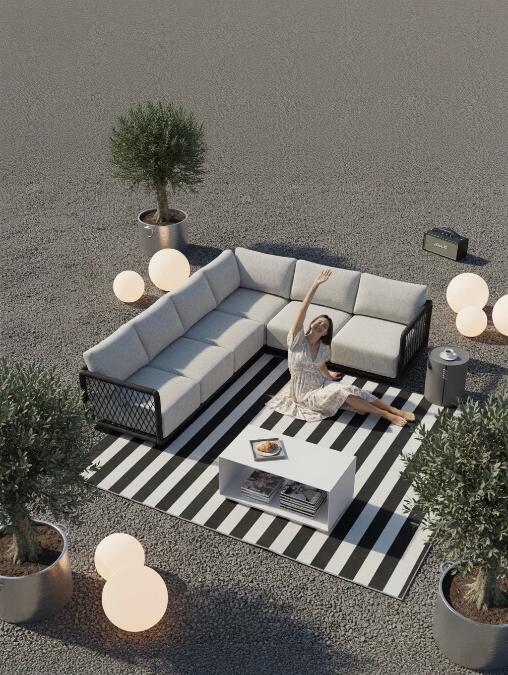 Mykonos Garten Ecklounge Set, 2er-Set auf einem schwarz-weiß gestreiften Teppich, ergänzt durch eine Frau in einem Blumenkleid, die entspannt sitzt. Umgebung mit sanft leuchtenden Kugellampen und Olivenbäumen.
