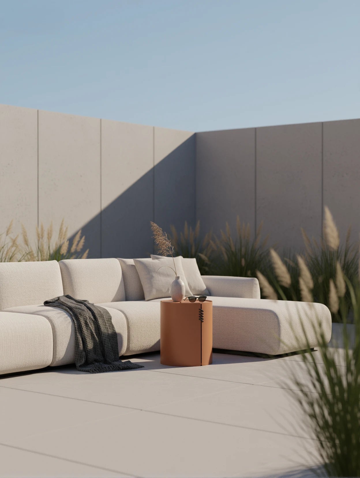 Babymax L-Lounge Set, 3er-Set: Ein modularer, cremefarbener Outdoor-Sofa mit passenden Kissen, abgerundet durch einen dunklen Wurf. Dazu ein zylindrischer Beistelltisch mit Vase und Sonnenbrille.