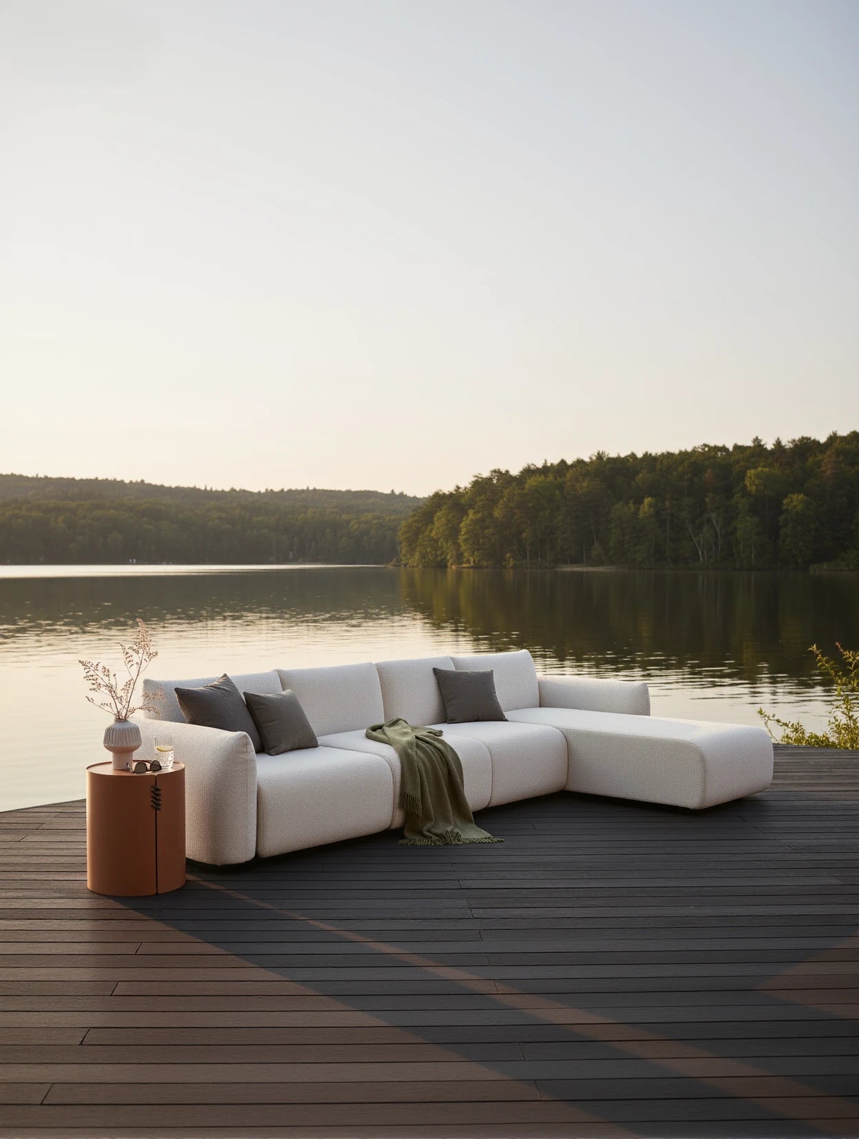 Das Babymax L-Lounge Set, 3er-Set, steht auf einem Holzdeck am See, bestehend aus einem weißen, modularen Sofa mit grauen Kissen und grünem Wurf, ideal für stilvolle, nachhaltige Entspannung im Freien.
