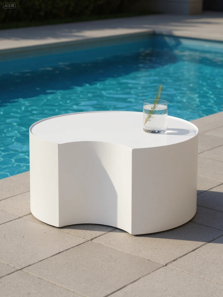 Speyer Crescent Couchtisch - Aluminium pulverbeschichtet-Weiß, steht am Pool, mit einem Wasserglas und Kräuterzweig darauf. Der skulpturale Tisch ergänzt stilvoll die Outdoor-Ästhetik von Finqa GmbH.
