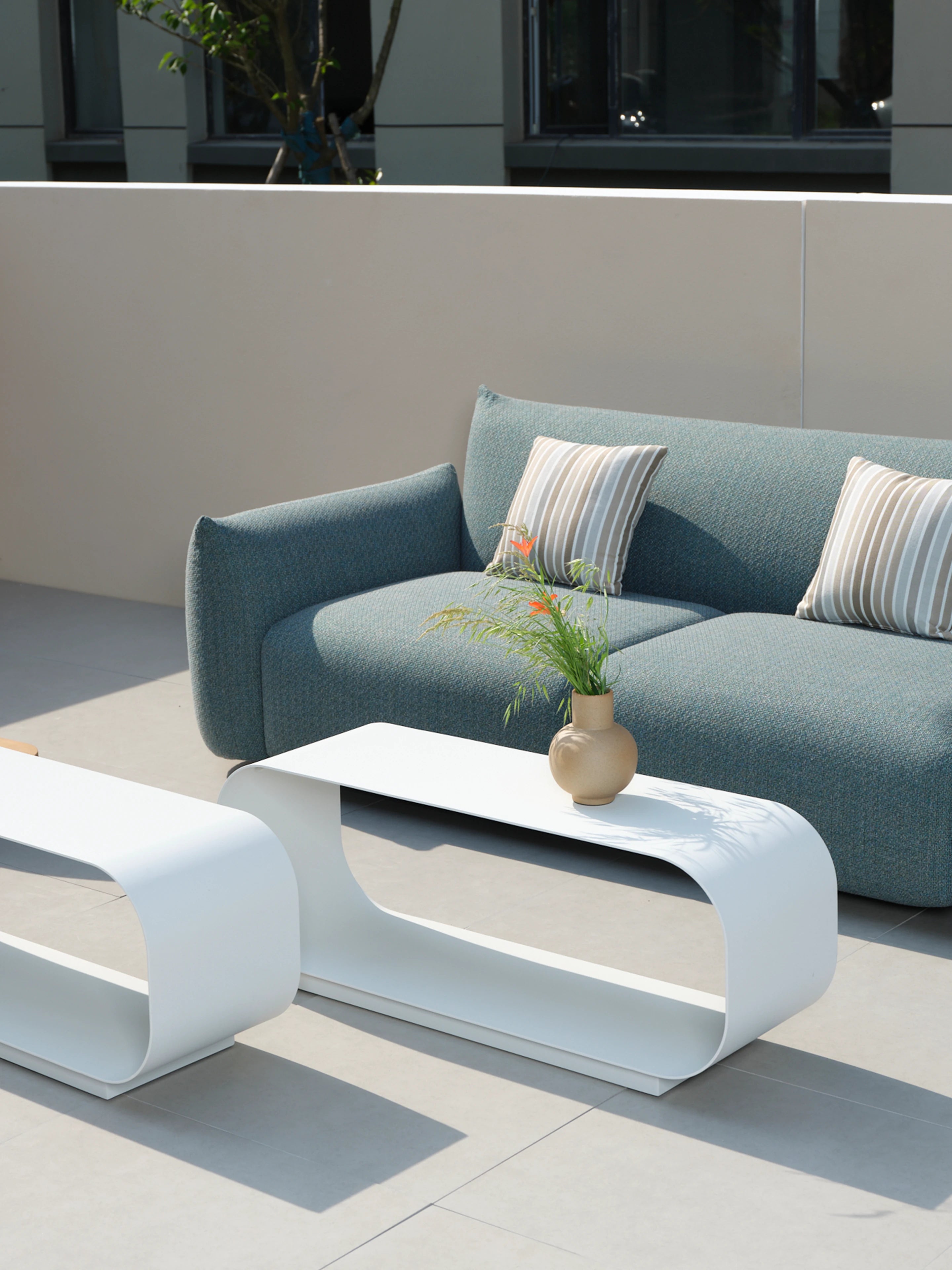 Leiden Ovaler ausgehöhlter Couchtisch im minimalistischen Außenbereich, ergänzt durch eine kleine Vase mit Grün und Blumen. Ein modernes, elegantes Design der Marke Finqa, das Leichtigkeit und Funktionalität vereint.