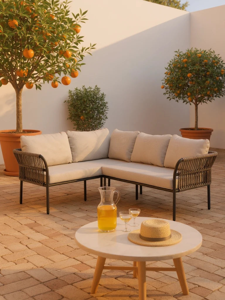 Malaga Garten Ecklounge Set (4-Sitzer) auf sonnigem Patio mit L-förmigem, geflochtenem Sofa, weißen Kissen, rundem Tisch mit Glaskaraffe und Zitronenbäumen in Terrakottatöpfen. Ideal für stilvolle, flexible Terrassengestaltung.