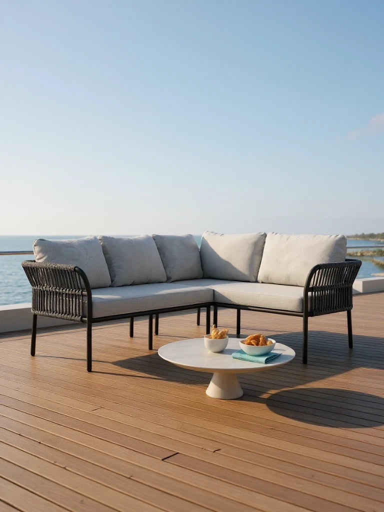 Malaga Garten Ecklounge Set (4-Sitzer) auf einer Terrasse am Meer, mit hellgrauem, L-förmigem Sofa und rundem, weißen Tisch mit Gebäck, repräsentiert Finqa GmbHs stilvolle, wetterfeste Outdoor-Möbel.