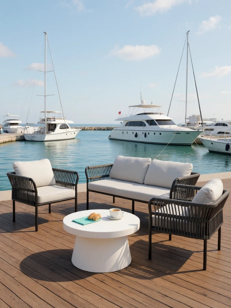 Malaga Garten Ecklounge Set (4-Sitzer) auf Holzterrasse mit modernen Sesseln, Sofa mit hellgrauen Polstern und rundem weißen Tisch, umgeben von ruhigem Wasser und Yachten im Hintergrund.