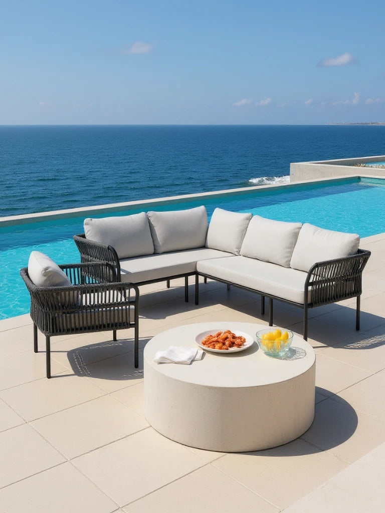 Malaga Garten Ecklounge Set (5-Sitzer) mit L-förmigem Sofa in schwarzem Rahmen und hellen Kissen, passendem Sessel, neben einem zylindrischen Tisch, vor einem Infinity-Pool mit Meerblick.