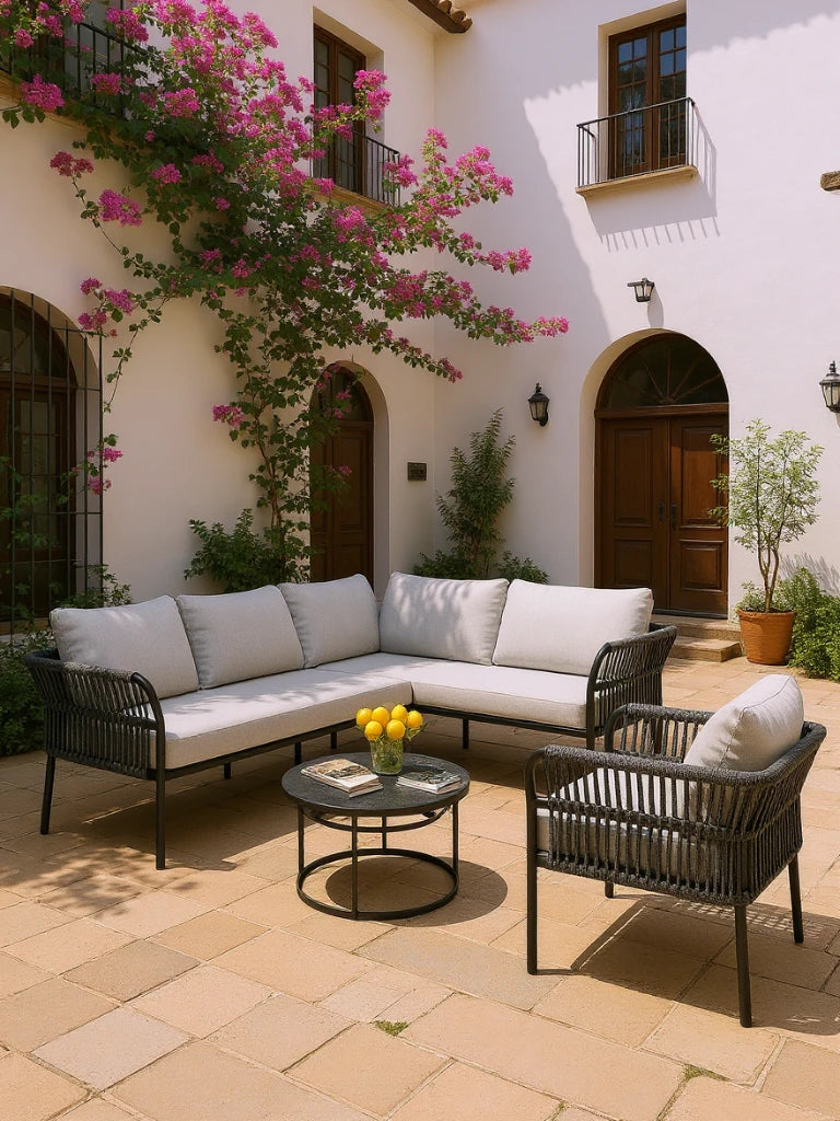 Malaga Garten Ecklounge Set (5-Sitzer) auf einer mediterranen Terrasse mit hellem Fliesenboden, weißen Wänden und Bougainvillea. Das Set besteht aus einem L-förmigen Sofa und Sessel mit grauen Kissen.