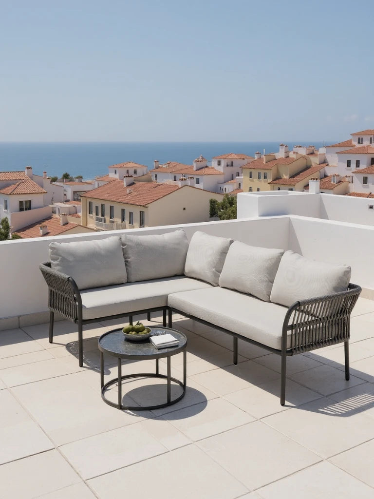 Malaga Garten Ecklounge Set (4-Sitzer) auf einer sonnigen Terrasse, bestehend aus einem L-förmigen Sofa mit grauen Kissen und einem runden Tisch, ideal für stilvolle, wetterfeste Outdoor-Einrichtungen.