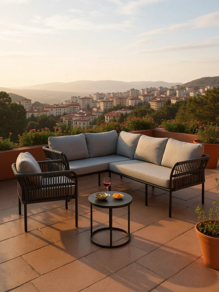 Malaga Garten Ecklounge Set (5-Sitzer) auf einer Terrasse bei Sonnenuntergang, bestehend aus einem L-förmigen Sofa, einem Sessel und einem Tisch mit Wein und Snacks, umgeben von blühenden Pflanzen.