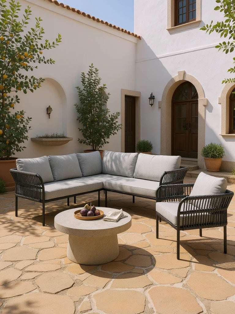 Malaga Garten Ecklounge Set (5-Sitzer) in einem mediterranen Innenhof mit L-förmigem Sofa und Sessel, schwarzem Metall-Rahmen, runder Steintisch mit Feigen, ideal für stilvolle, wetterfeste Terrassenmöbel.