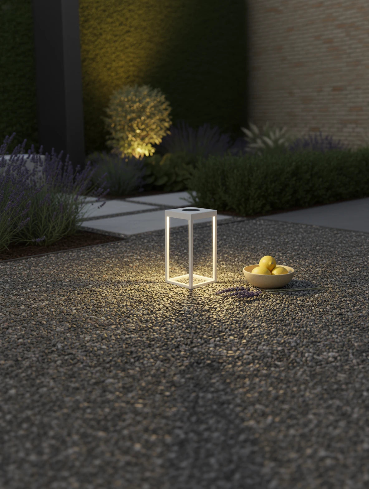 Kenya Solar Gartenlampe auf einem Kieselstein-Patio, strahlt warmes Licht aus, neben einer Schale mit Zitronen und Lavendel, betont modernes, nachhaltiges Design von Finqa GmbH für stilvolle Außenbereiche.