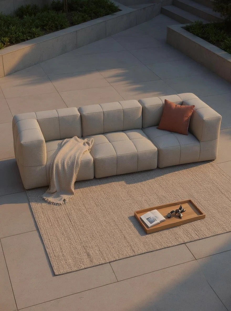 Modulares Garten-Lounge-Set Marshmallow, 3er-Set auf einer steinernen Terrasse, mit weichem Wurf, Akzentkissen und Zubehör auf einem Naturfaserteppich, im Sonnenlicht.