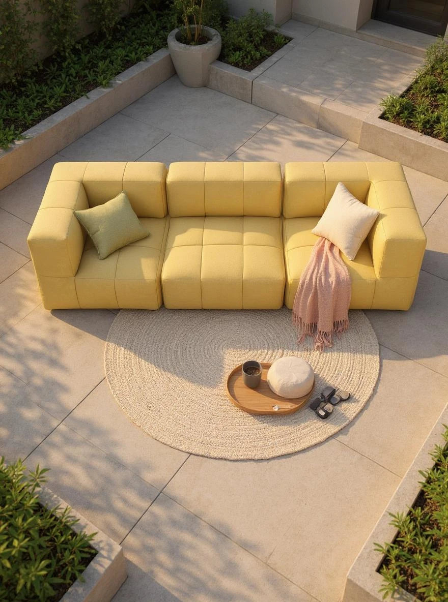Modulares Garten-Lounge-Set Marshmallow, 3er-Set: Ein gelbes, modulares Sofa aus drei kubischen Elementen mit Armlehnen, ergänzt durch Kissen und Decke, auf einem modernen, minimalistischen Außenbereich mit Naturakzenten.