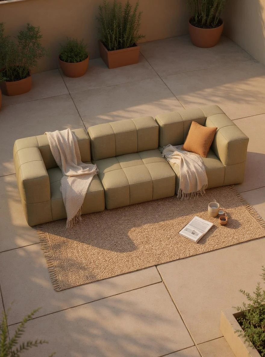Modulares Garten-Lounge-Set Marshmallow, 3er-Set, auf einer Terrasse: Olivefarbenes, L-förmiges Sofa mit Decken und Kissen, umgeben von Keramiktassen und Pflanzgefäßen, für stilvolles, nachhaltiges Outdoor-Entspannen.