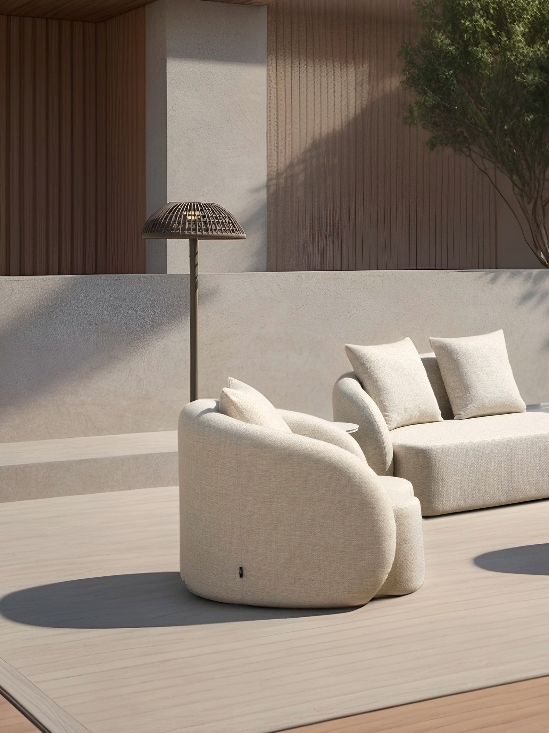 Kapalai Vertikale Lampe Aluminium Pulverbeschichtung Olefin- Taupe steht links neben einem minimalistischen Outdoor-Set auf einer Holzterrasse, ergänzt durch eine organische Form und hochwertigen Materialien.