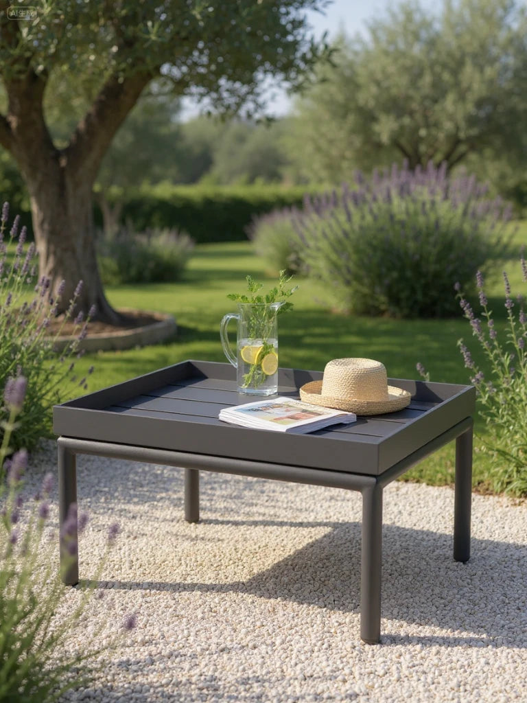 Amsterdam Lounge-Lodi Aluminium-Couchtisch auf heller Kieselterrasse im sonnigen Garten, dekoriert mit Glaskrug, Strohhut und Magazin. Perfekt für stilvolle Outdoor-Essumgebung, leicht zu reinigen und flexibel.