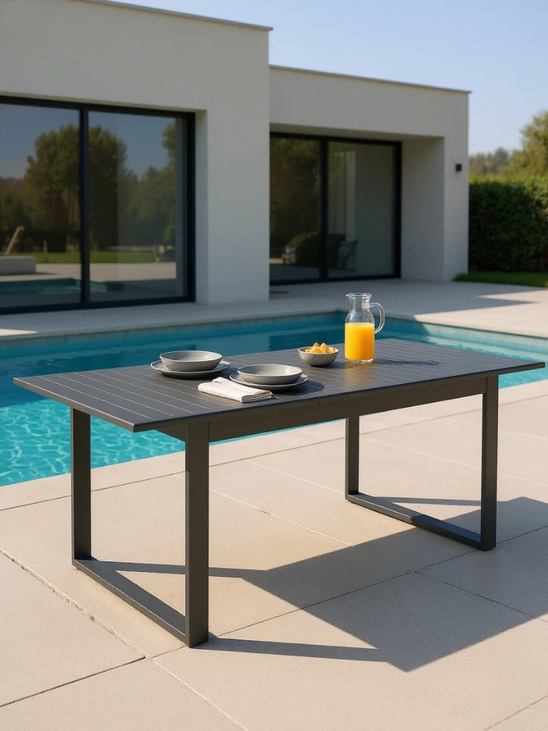Warschau Ausziehbarer Esstisch Aluminium-Pulverbeschichtung Rechteckig Dunkelgrau auf Poolterrasse, gedeckt mit Krug, Schalen und Serviette, vor modernem Haus und Pool, ideal für stilvolle Outdoor-Dining-Erlebnisse.