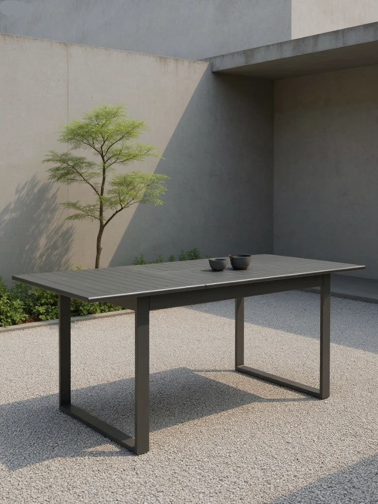 Warschau Ausziehbarer Esstisch Aluminium-Pulverbeschichtung Rechteckig Dunkelgrau, minimalistisch in einem sonnenbeschienenen Innenhof, ergänzt durch zwei schwarze Keramikschalen, verkörpert elegantes Design und Funktionalität für den Außenbereich.