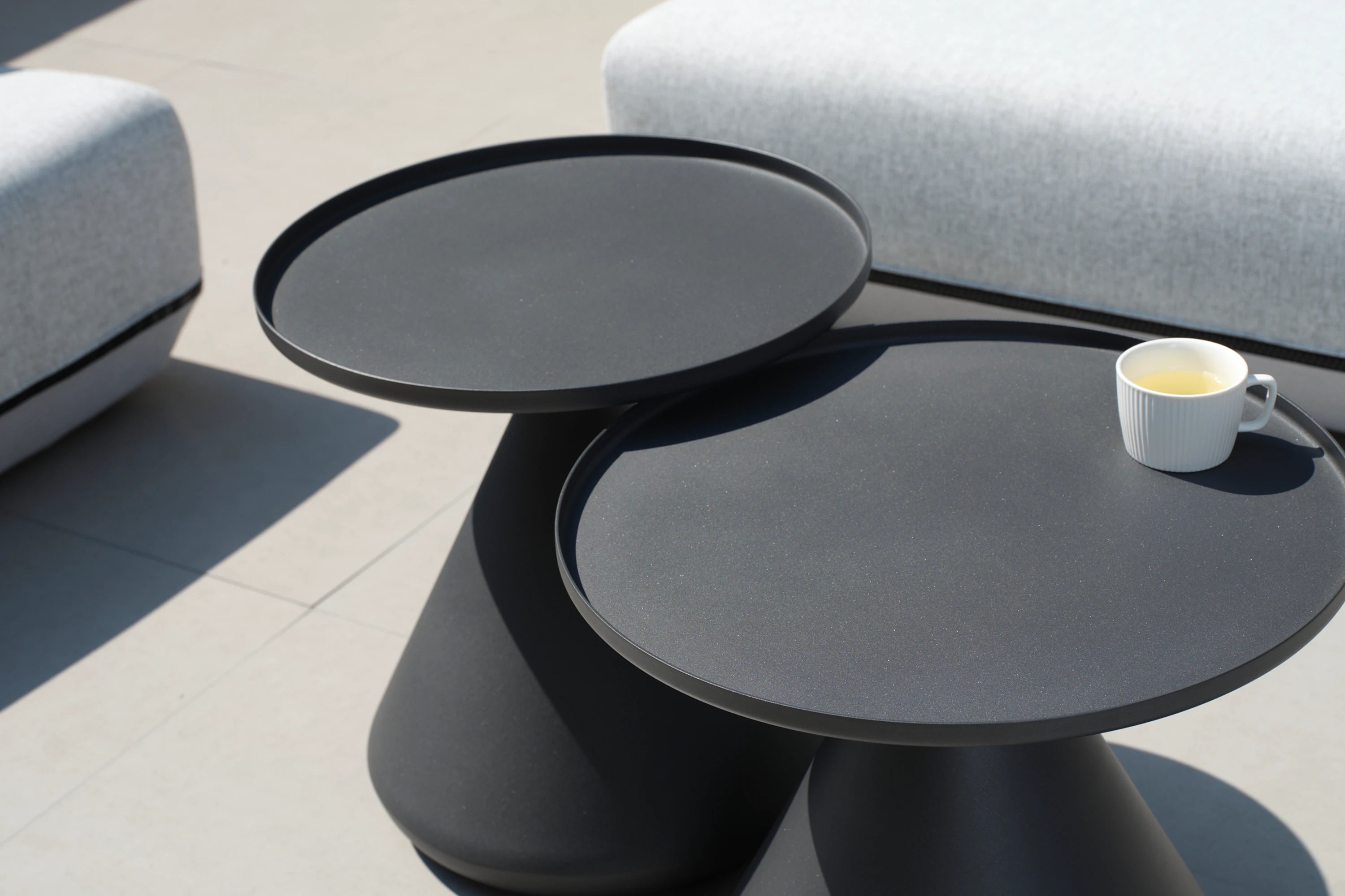 Aluminium-Rundtisch mit beschwertem Sockel, präsentiert auf weißer Fläche mit einer Tasse darauf. Elegantes Design, passend zu Finqa GmbH's nachhaltigen, stilvollen Outdoor-Möbeln für flexible Gartengestaltung.