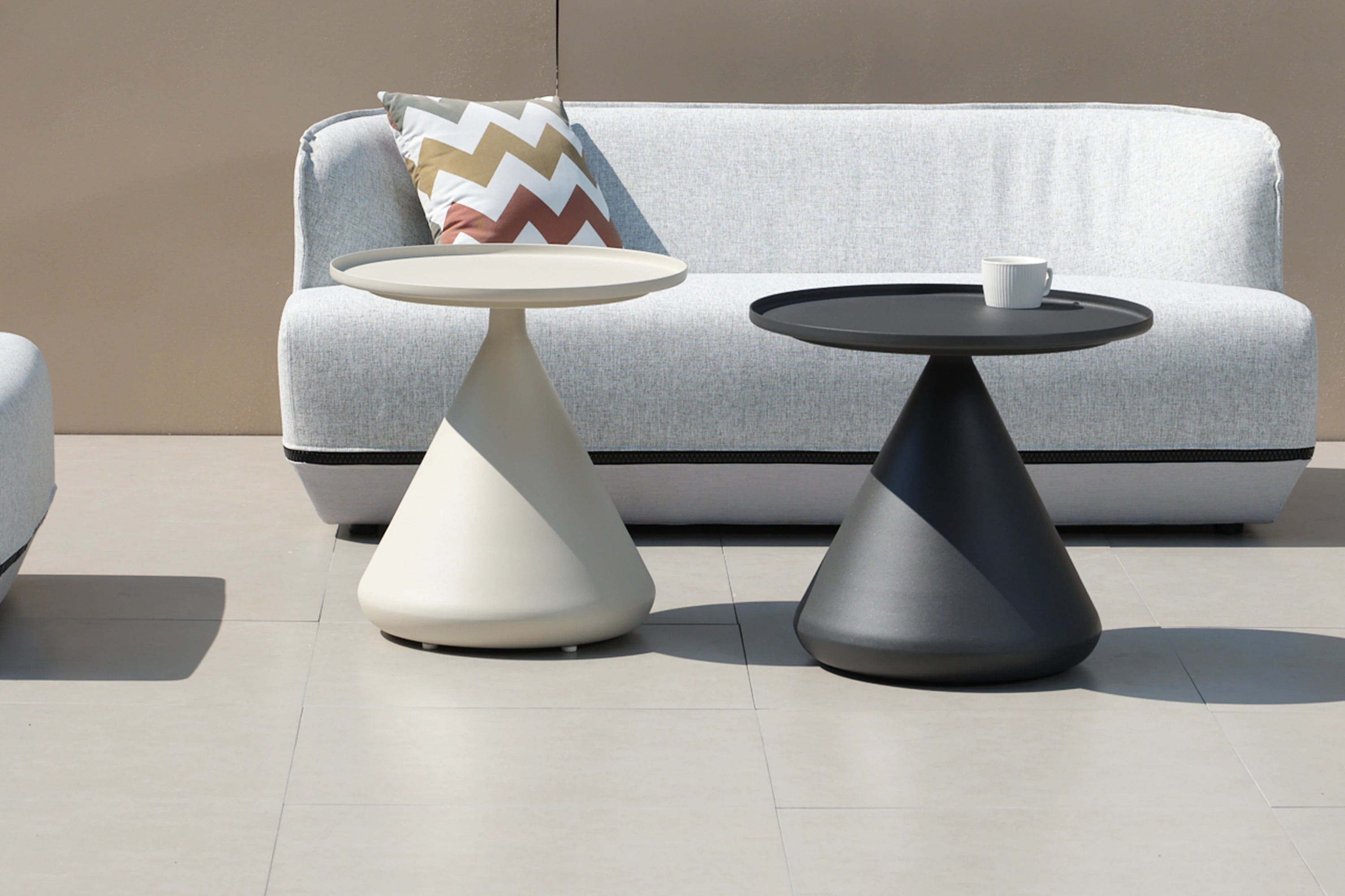 Aluminium-Rundtisch mit schwerem Sockel, neben einem Sofa platziert. Auf dem Tisch steht eine weiße Tasse. Perfekt für stilvolle, modulare Outdoor-Designs von Finqa GmbH.