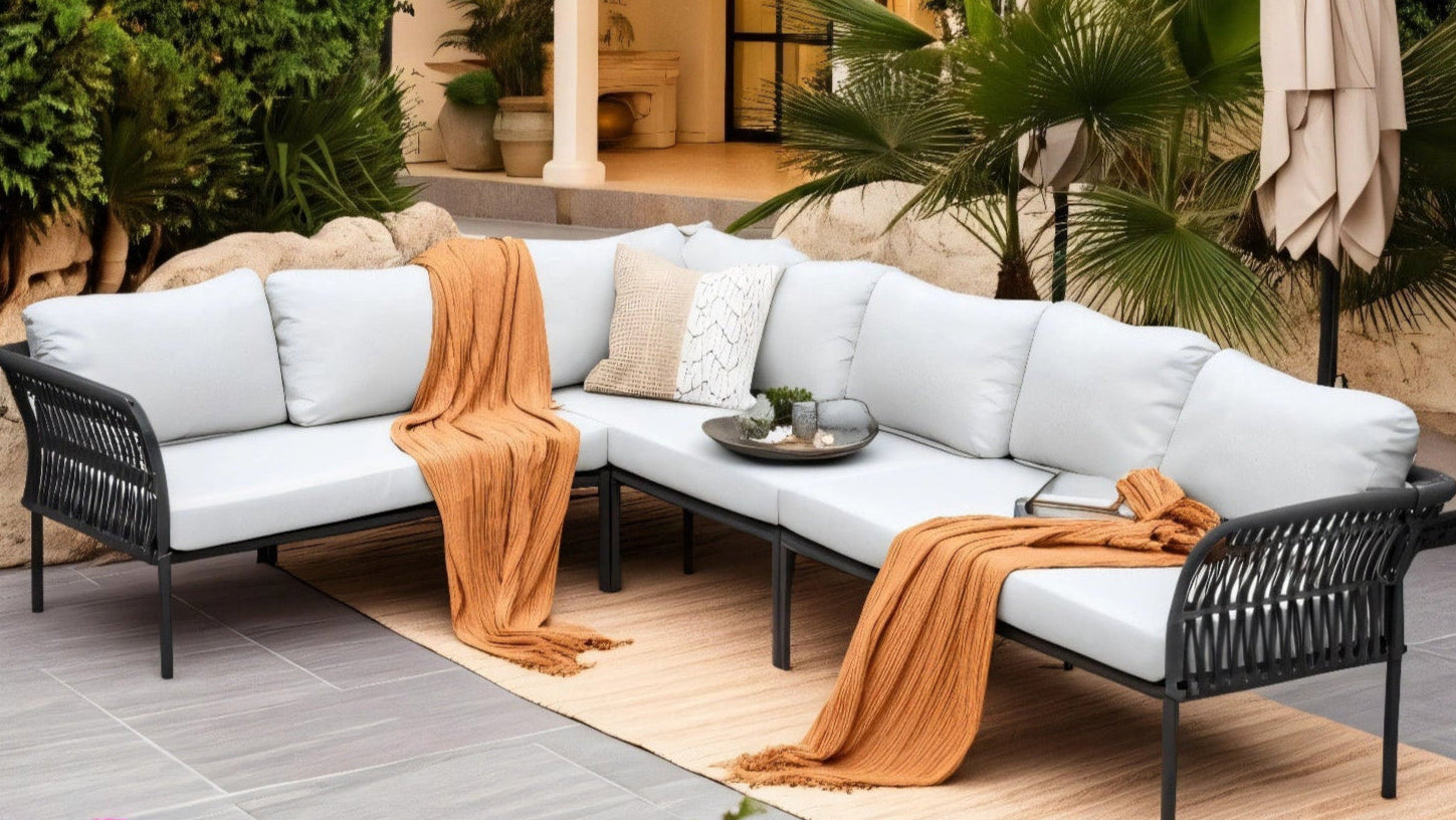 Malaga Garten Ecklounge Set (5-Sitzer) auf einer Terrasse, bestehend aus einem weißen Sofa mit orangenen Decken und Kissen, umgeben von stilvollen Accessoires wie Pflanzen und einer Skulptur.