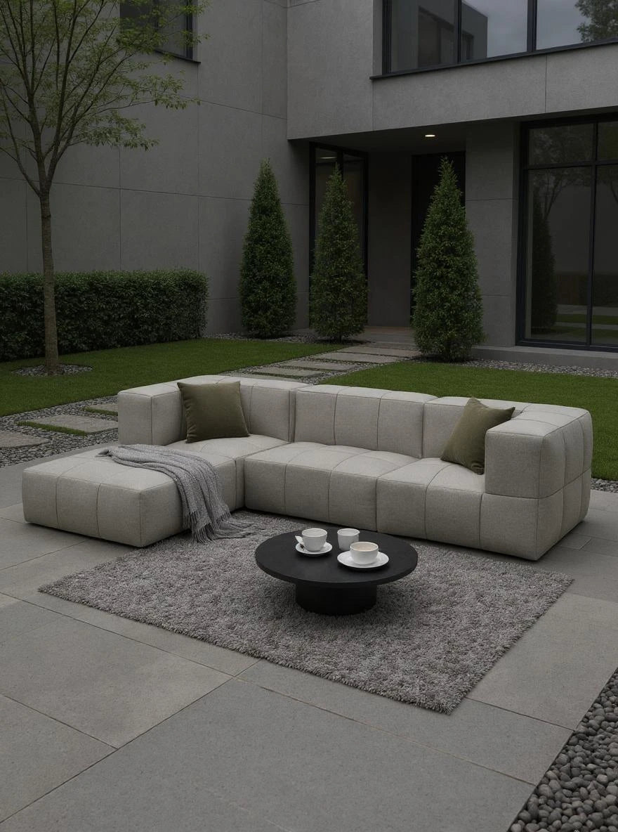Babymax, 4er-Set: L-förmiges, niedriges Sofa im modernen Patio, ergänzt durch grüne Kissen und Decke, präsentiert auf grauem Teppich mit Kaffeetisch, stilvoll eingebettet in gepflegter Gartenumgebung.