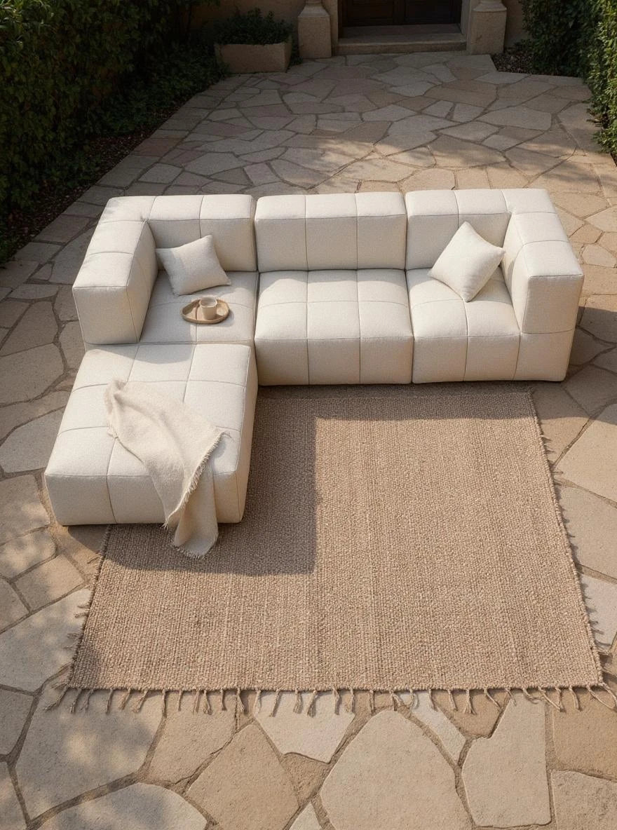 Babymax, 4er-Set (Copy), ein modulares, cremefarbenes L-förmiges Sofa mit Fransenwolldecke und zwei Kissen, auf einer Jutematte im Freien; zeigt Finqas nachhaltiges, designorientiertes Outdoor-Möbelangebot.