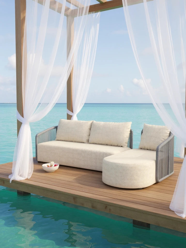 Kapalai Garten Loungesofa Set (4-Sitzer) auf einem Holzdeck über türkisfarbenem Wasser. L-förmiges Sofa mit Ottomane, unter Pergola mit weißen Vorhängen, betont Komfort und stilvolle Entspannung.