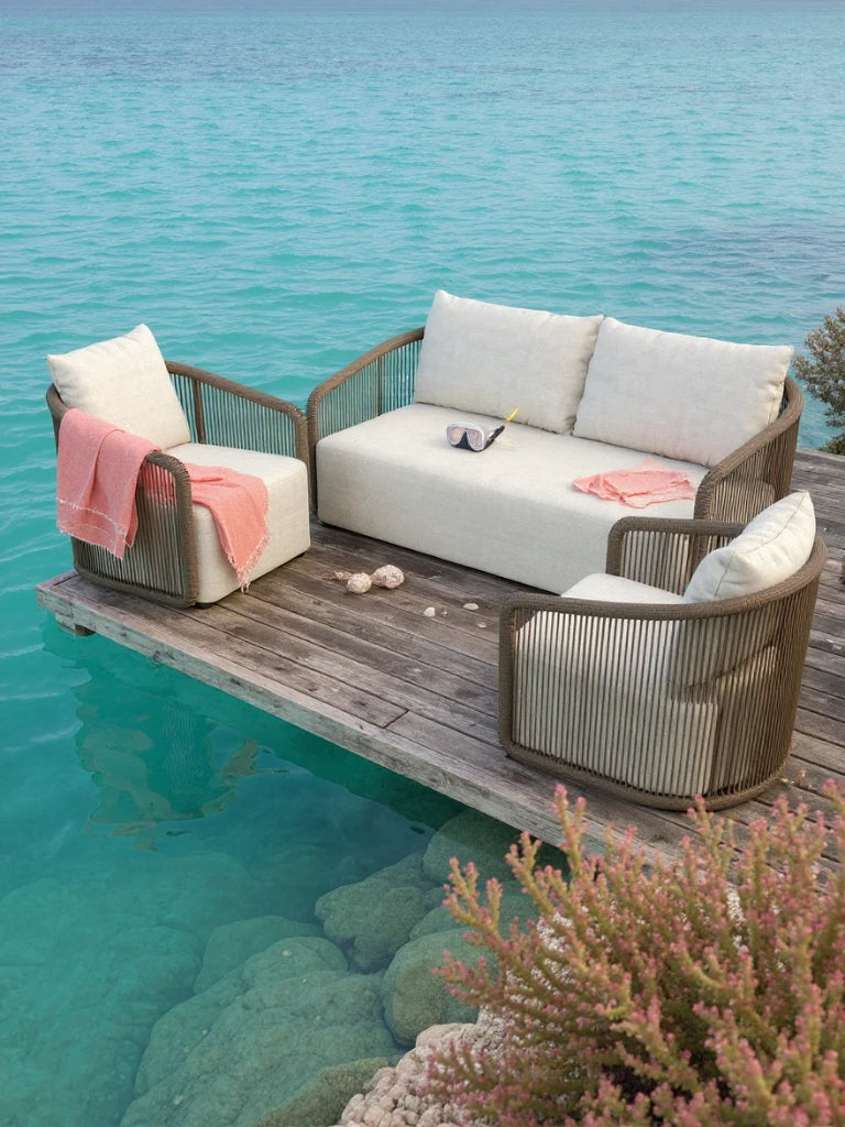 Kapalai Garten Loungesofa Set (4-Sitzer) auf einem Holzdeck über türkisblauem Wasser, bestehend aus einem Sofa und zwei Sesseln mit weißen Kissen, verziert mit korallfarbenen Decken und einem Schnorchelmasken-Detail.