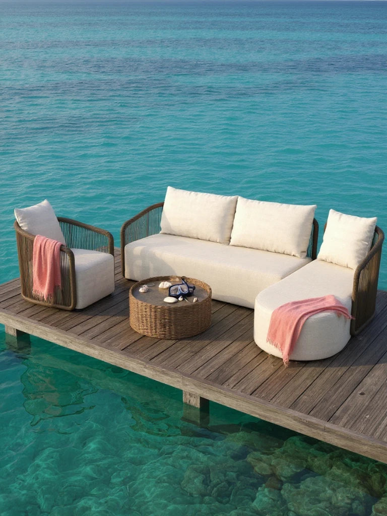 Kapalai Garten Loungesofa Set (5-Sitzer) auf einem Holzsteg über türkisblauem Wasser, bestehend aus einem Sessel, drei-Sitzer Sofa und geschwungenem Chaiselongue, mit pinken Decken und einem runden Tisch.
